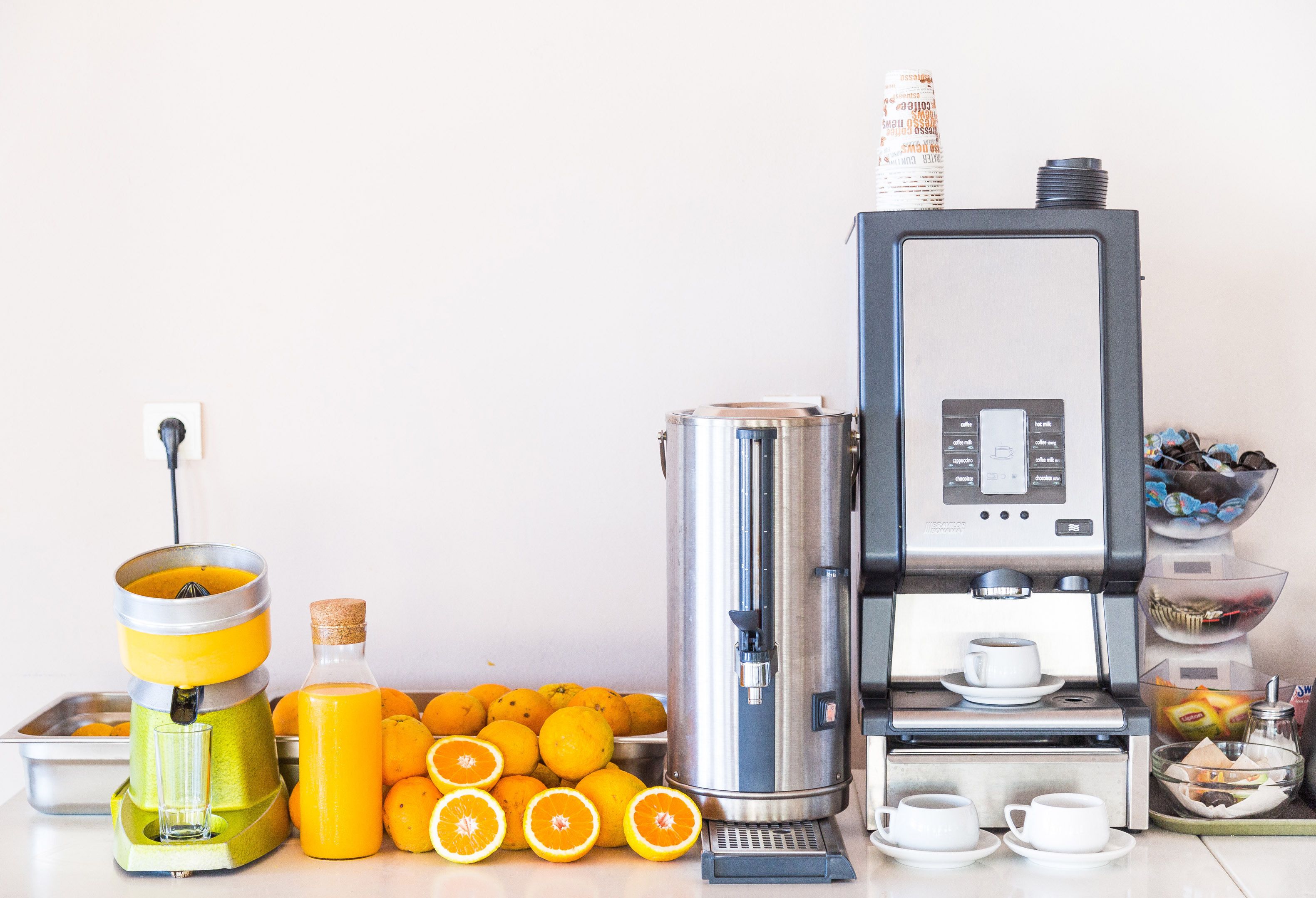 Una cocina con exprimidor, máquina de café y un cuenco de naranjas.