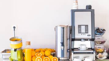 Una cocina con exprimidor, máquina de café y un cuenco de naranjas.