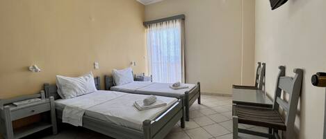 Habitación de hotel con dos camas individuales, un escritorio, una silla, un televisor y una ventana con cortinas.
