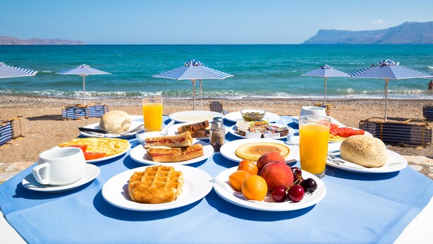 A breakfast setup on a beach with a view of the sea and mountains. - Galini Beach Hotel (Kissamos)