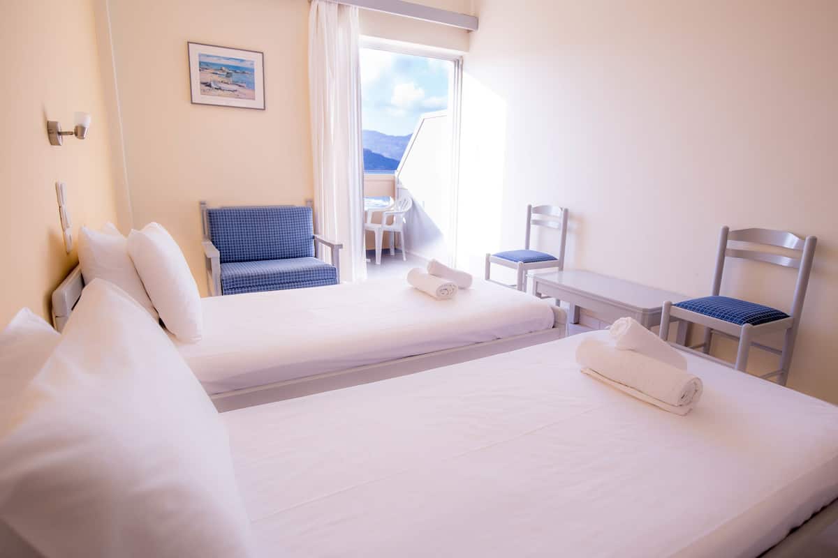 A hotel room with two beds, a desk, a chair, and a balcony with a view of the mountains.
