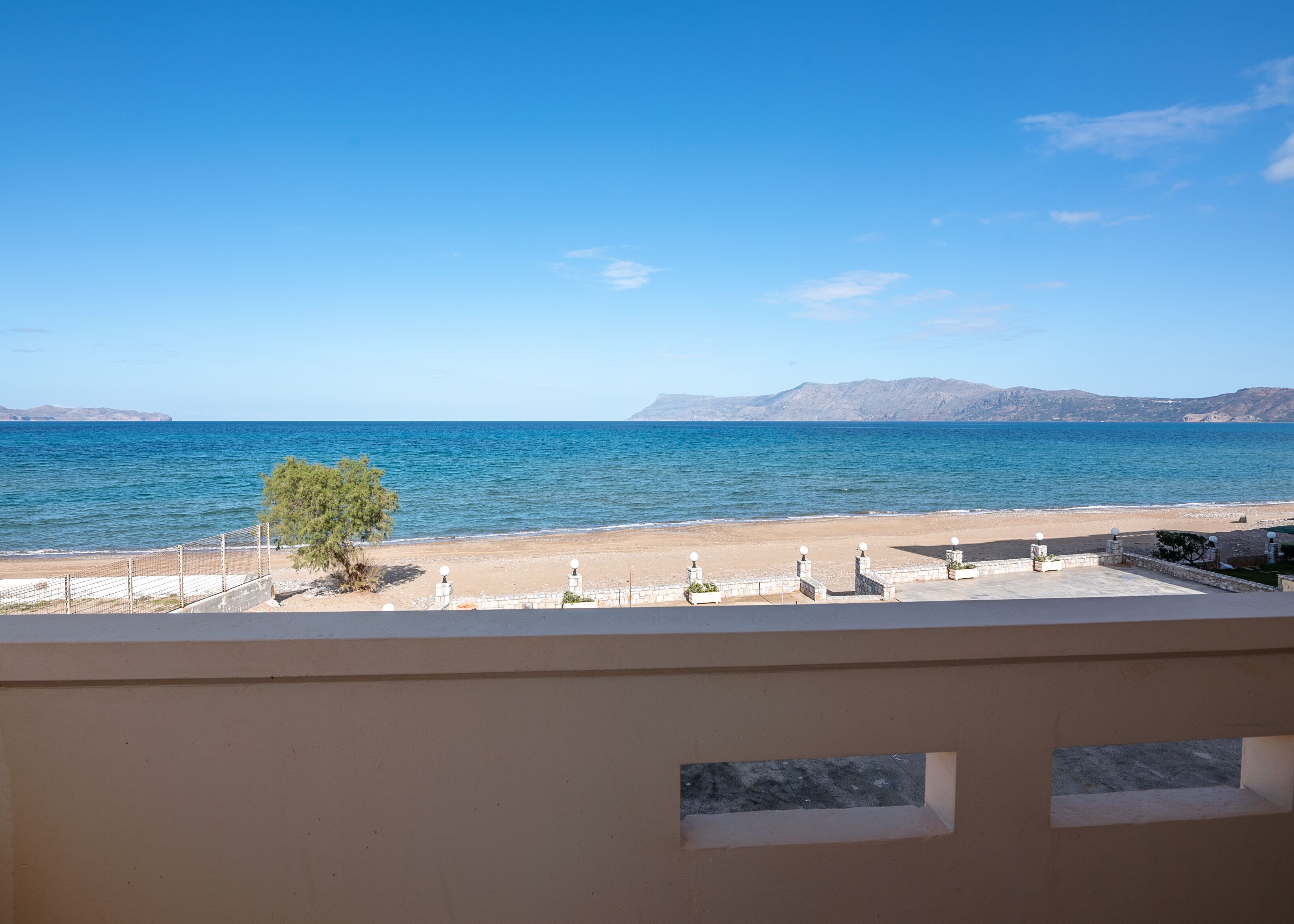 Vista de una playa con cielo despejado, orilla arenosa y montañas a lo lejos.