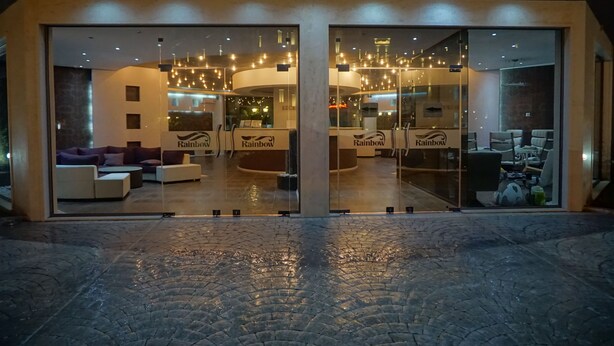 A modern hotel entrance with glass doors, a lounge area with sofas and a coffee table, and a visible sign reading "Rainbow". - Rainbow 3 Resort Club (Sunny Beach)