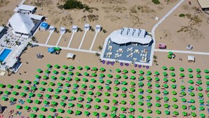 An aerial view of a beach resort with rows of green umbrellas, a parking area, and a building with a curved roof. - Rainbow 3 Resort Club (Sunny Beach)
