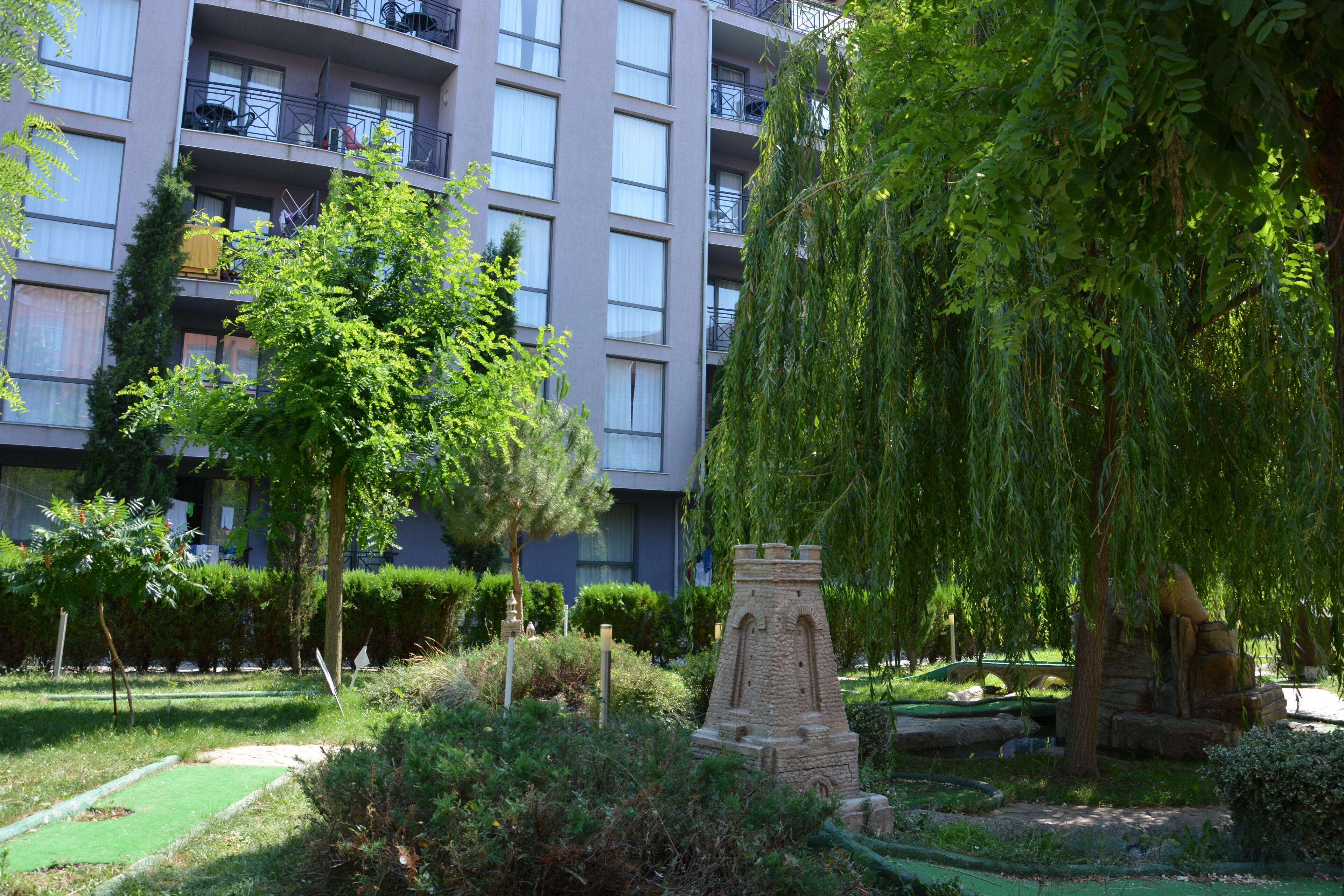 Une cour avec un monument en pierre, une végétation luxuriante et un immeuble à plusieurs étages doté de balcons.