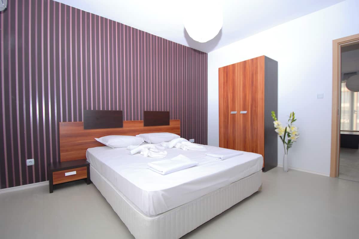 Quarto moderno com cama grande, cabeceira de madeira e mesa de cabeceira.