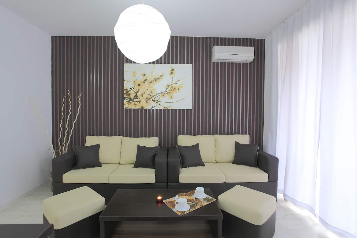 Uma sala de estar moderna com um sofá, uma mesa de centro com xícaras e um tabuleiro, e um ar condicionado fixado na parede.
