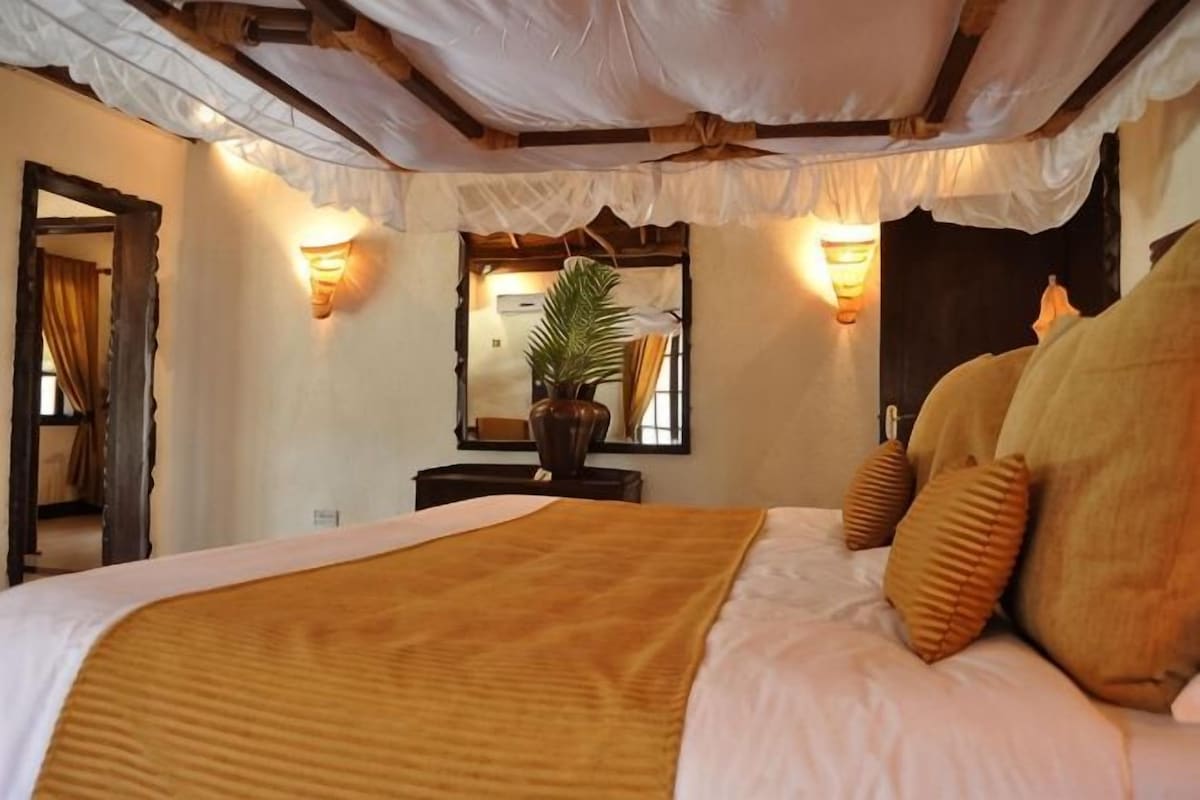 A bedroom with a large bed, a potted plant, and wall-mounted lights.