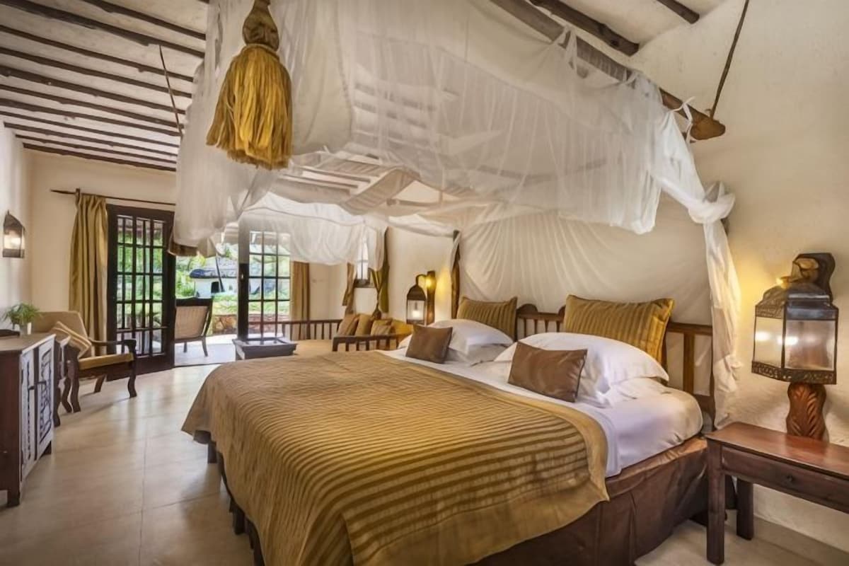 A bedroom with a canopy bed, bedside lamps, and a view of the outdoors.