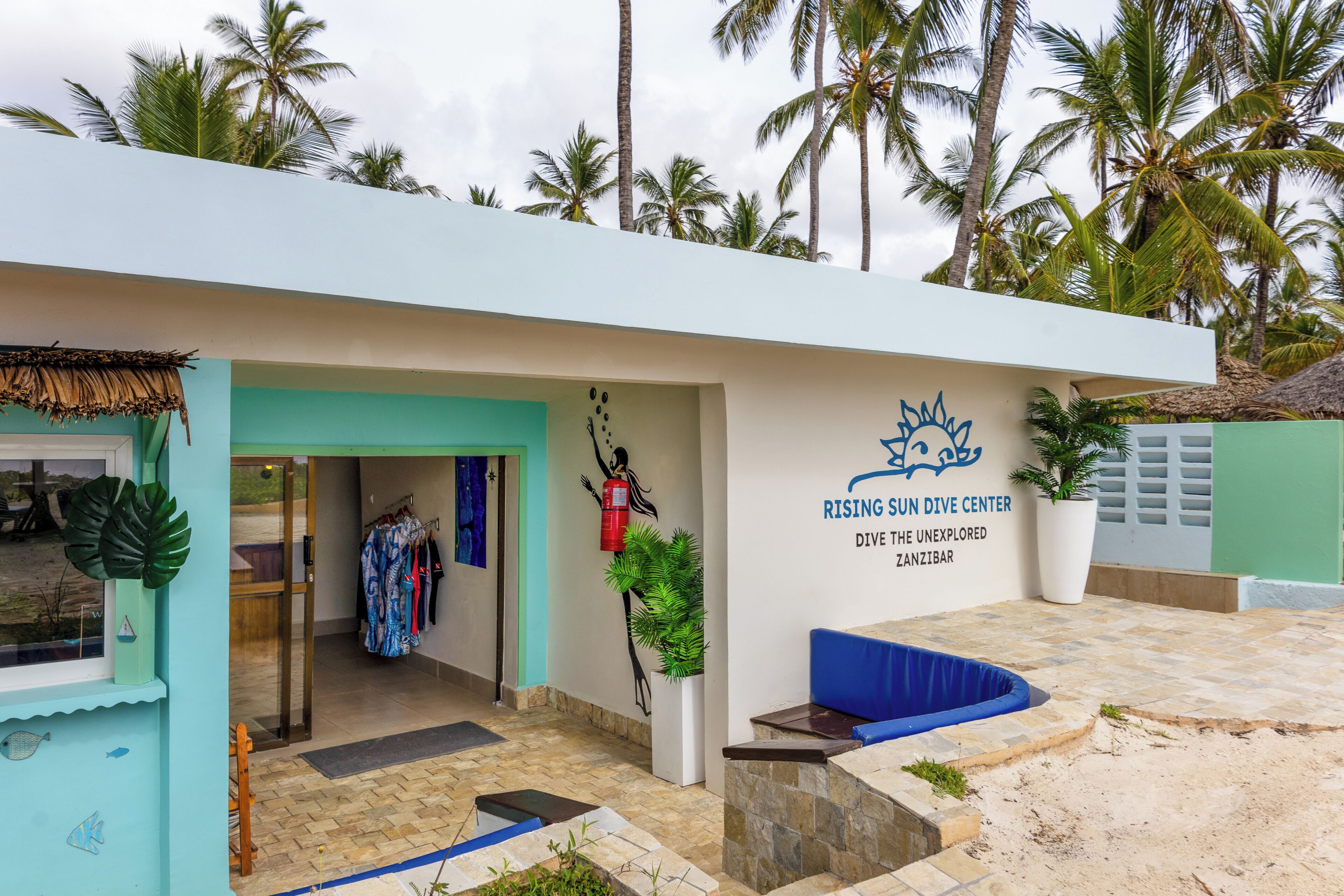 Un edificio con un letrero que dice 'RISING SUN Dive Center' y un área de recepción con un banco azul.