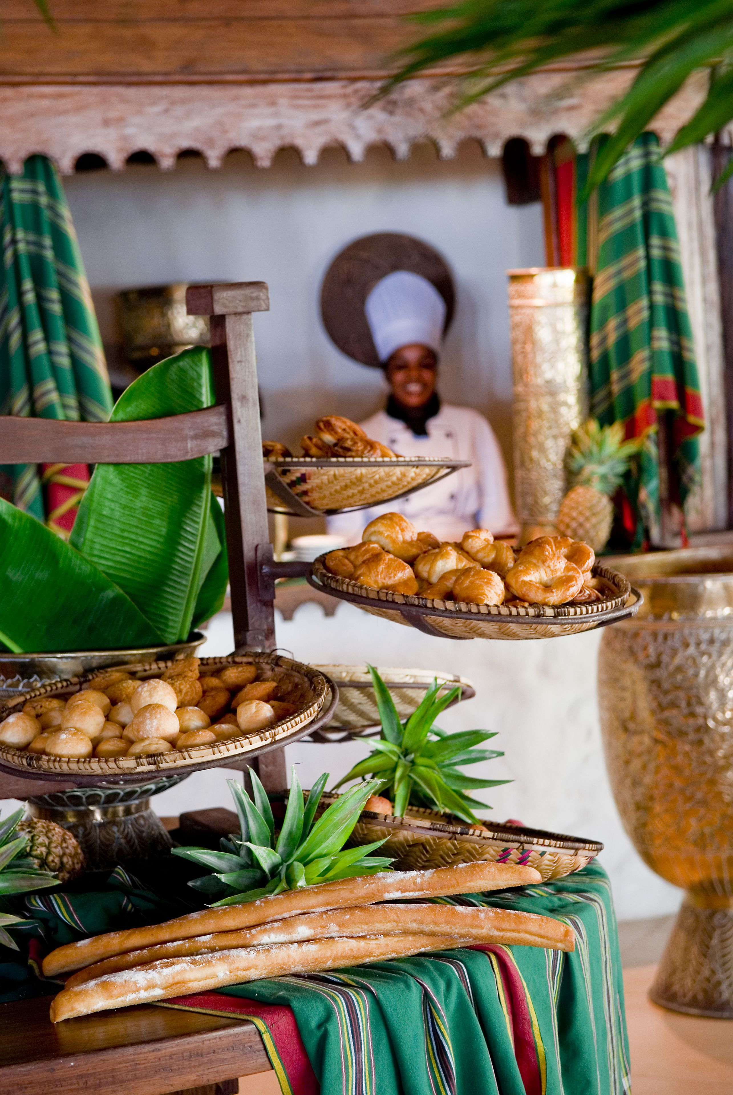 A traditional setting with a variety of baked goods displayed on tiered stands, a large decorative vase, and a person in the background.