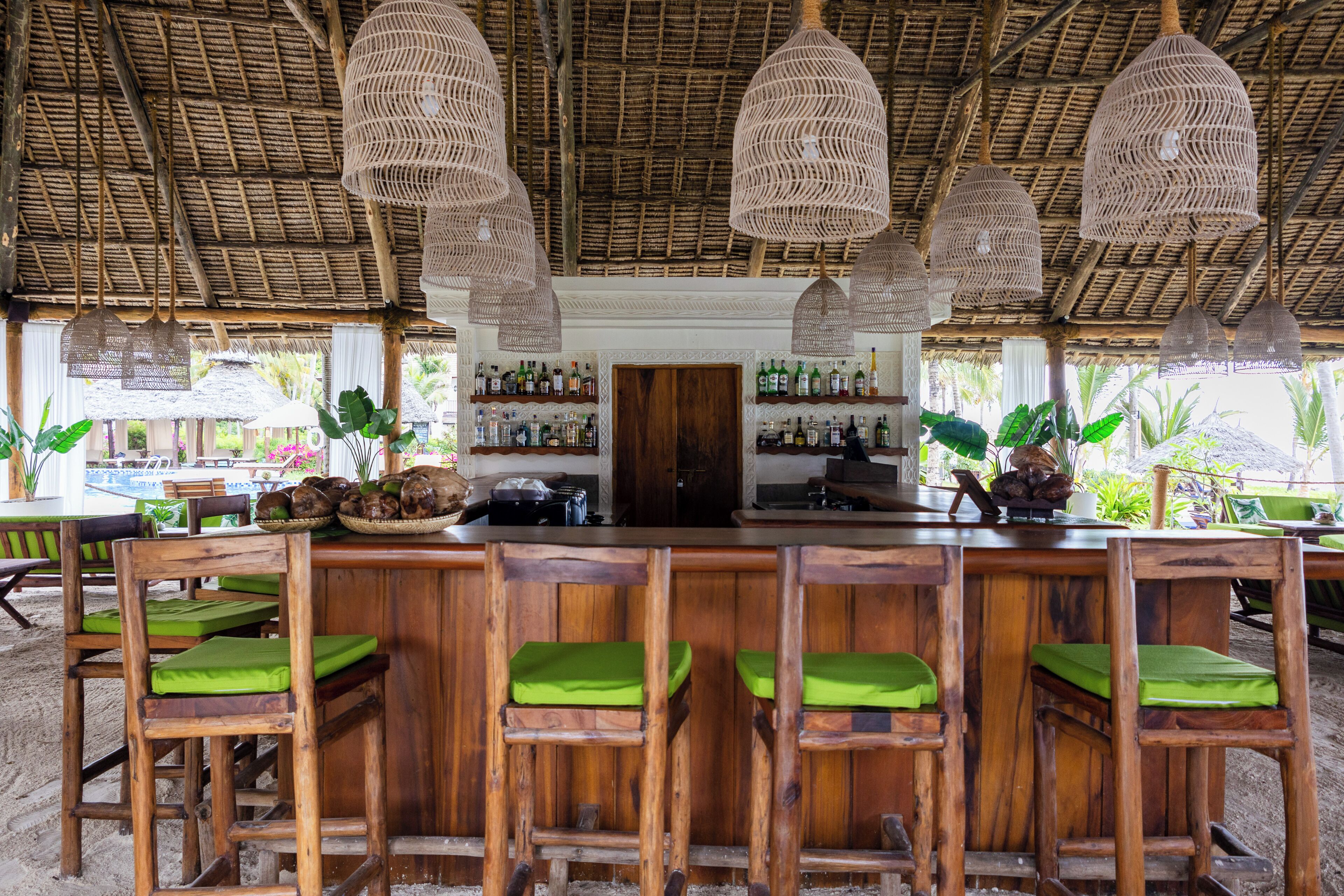 Una zona de bar con taburetes de madera y techo de paja.