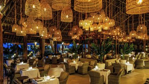 Un restaurant doté de meubles en osier, de luminaires suspendus et d’un plafond en chaume.