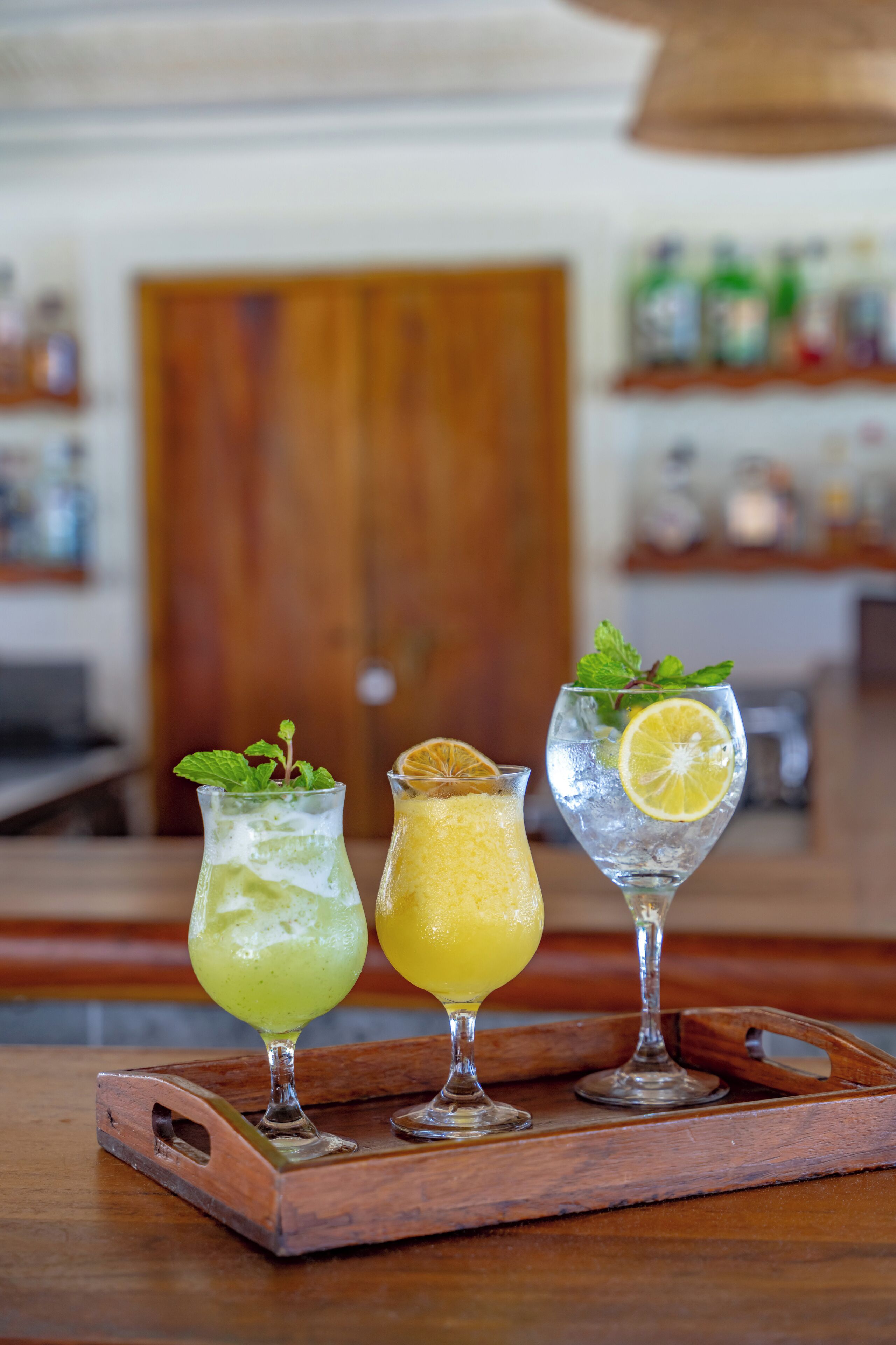 Three glasses of beverages on a wooden tray.