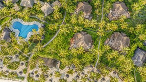 Vue aérienne d’un complexe hôtelier comprenant plusieurs bâtiments de style bungalow, une piscine centrale et une plage.
