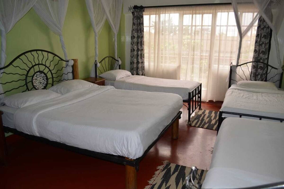 Una habitación con tres camas individuales, cada una con estructura de madera y ropa de cama blanca. El piso es rojo y las paredes son verdes.