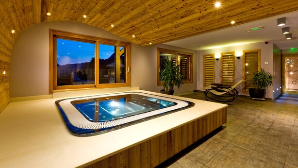 Un espace spa doté d’un jacuzzi, d’un plafond en bois et de grandes fenêtres.