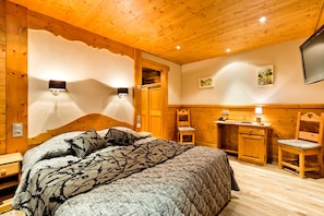 A cozy room with a wooden ceiling, a bed with a patterned blanket, a desk, and a chair. - Hôtel Beau Site (Saint-Jean-de-Sixt)