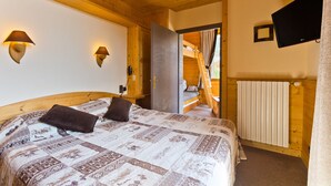 Une chambre à coucher aux murs lambrissés, comprenant un lit, deux lampes fixées au mur, un téléviseur et donnant sur une chambre en mezzanine.