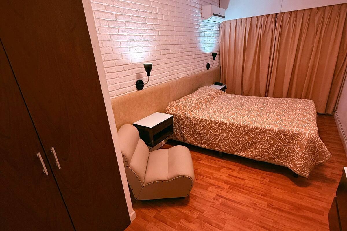 A compact room with a bed, a sofa, a wardrobe, and a brick wall.