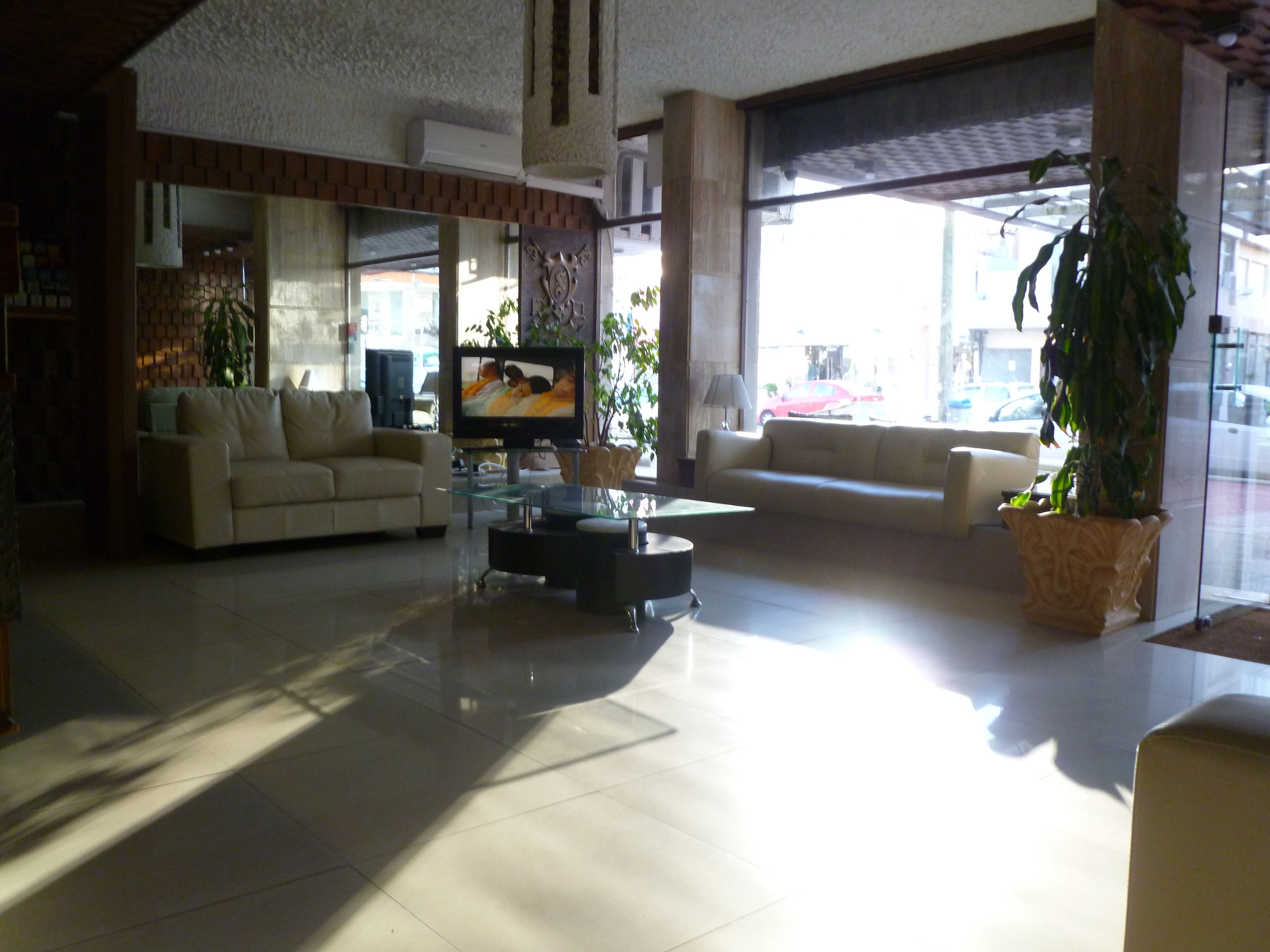 Ein geräumiger Wohnbereich mit zwei Sofas, einem Couchtisch und einem Fernseher. Große Fenster sorgen für natürliches Licht und Blick auf die Straße.