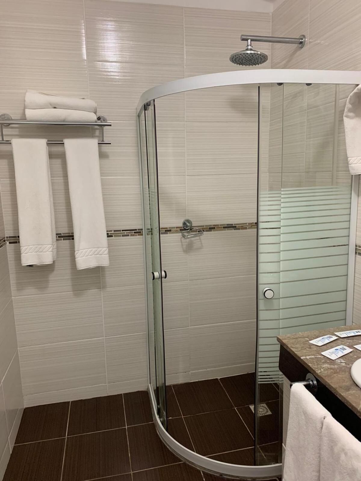 A modern bathroom with a glass shower enclosure, white tiled walls, and a brown floor.