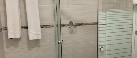 A modern bathroom with a glass shower enclosure, white tiled walls, and a brown floor.