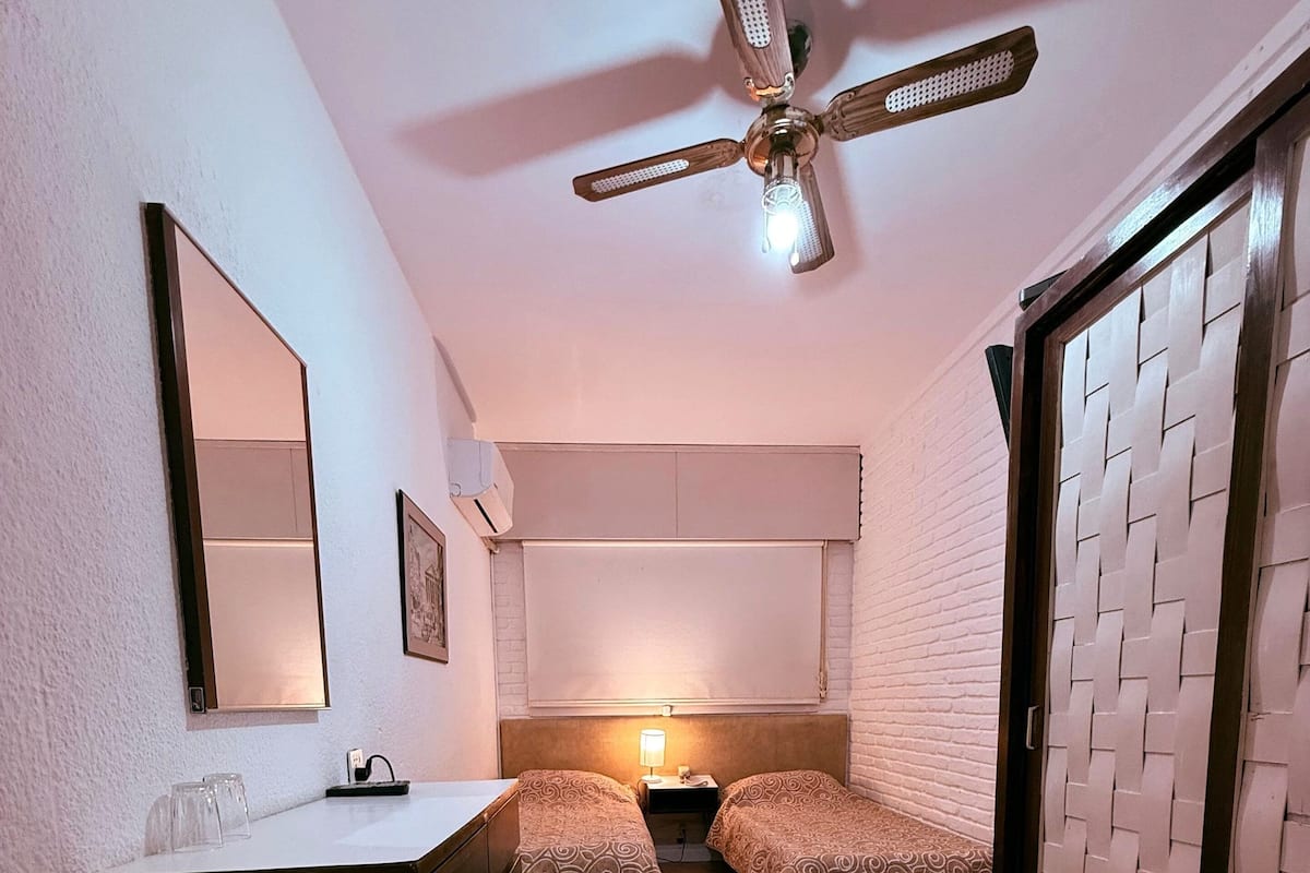 A compact room with two single beds, a ceiling fan, a small desk, and a wardrobe.
