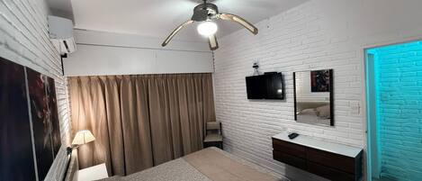 A bedroom with a bed, a ceiling fan, a TV, a mirror, and a blue-lit door.