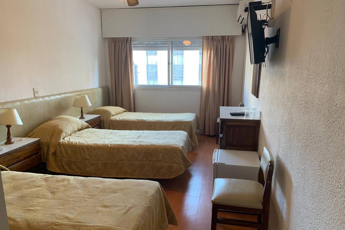 A hotel room with three beds, a desk, a chair, and a window with curtains.
