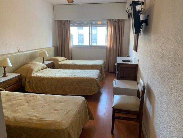 Habitación de hotel con tres camas, un escritorio, una silla y una ventana con cortinas.