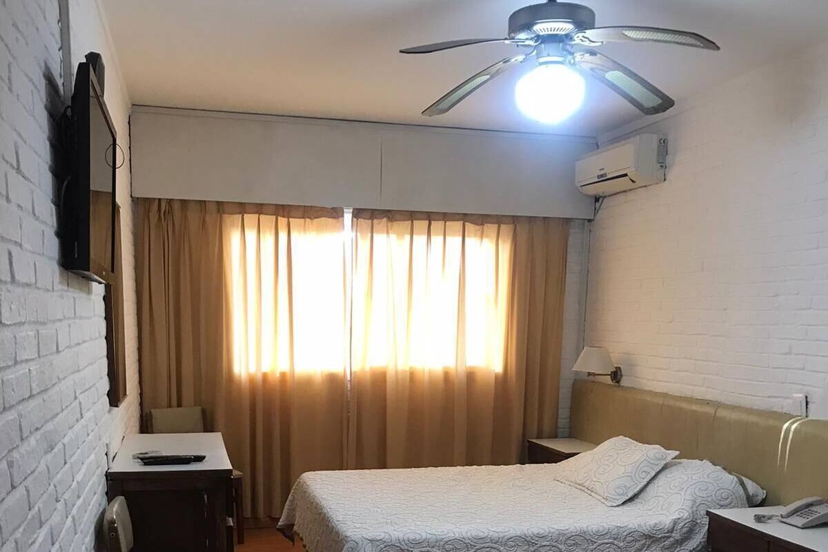 A hotel room with two beds, a desk, a chair, a ceiling fan, and a window with curtains.