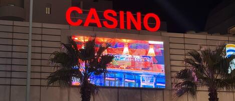 Un edificio de casino con un llamativo letrero rojo que dice 'CASINO', palmeras y una entrada muy iluminada.