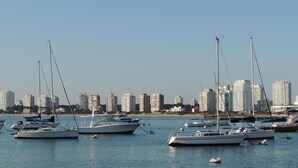A marina with several sailboats docked, a clear sky, and a city skyline in the background. - Shelton Hotel (Punta del Este)