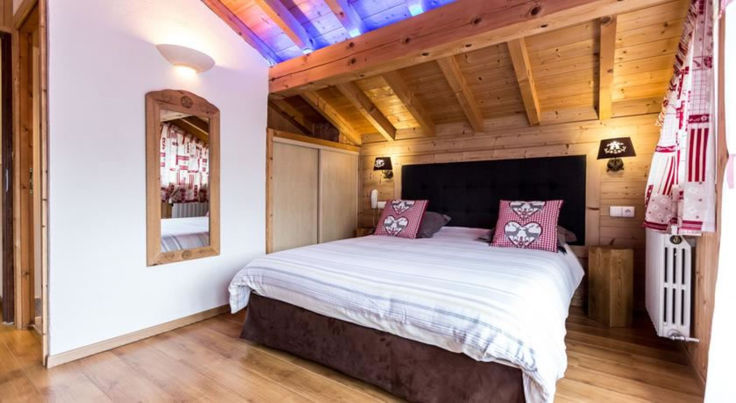 A wooden bedroom with a bed, two bedside tables, and a mirror.