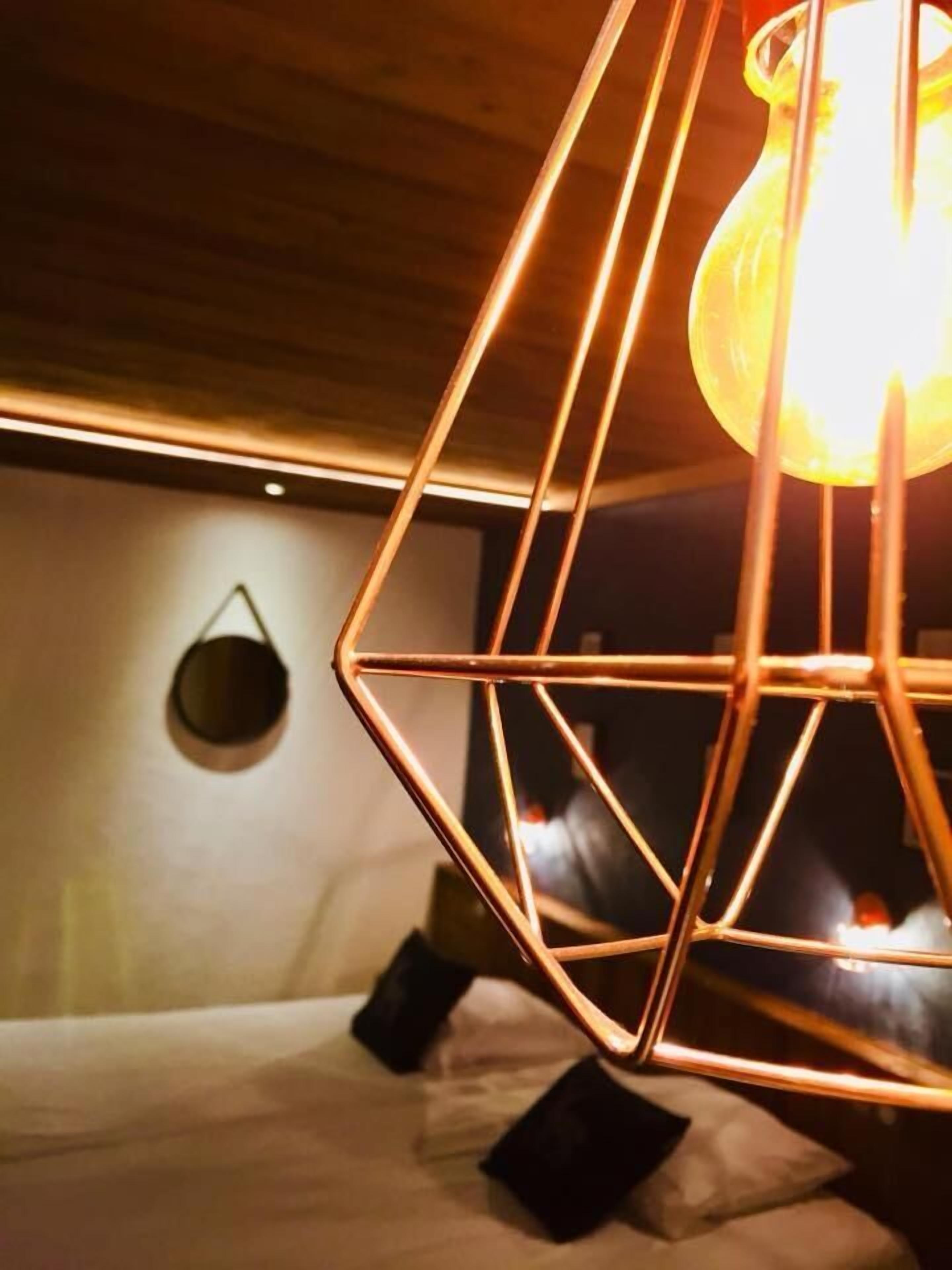 A room with a geometric metal light fixture and a bed with pillows.