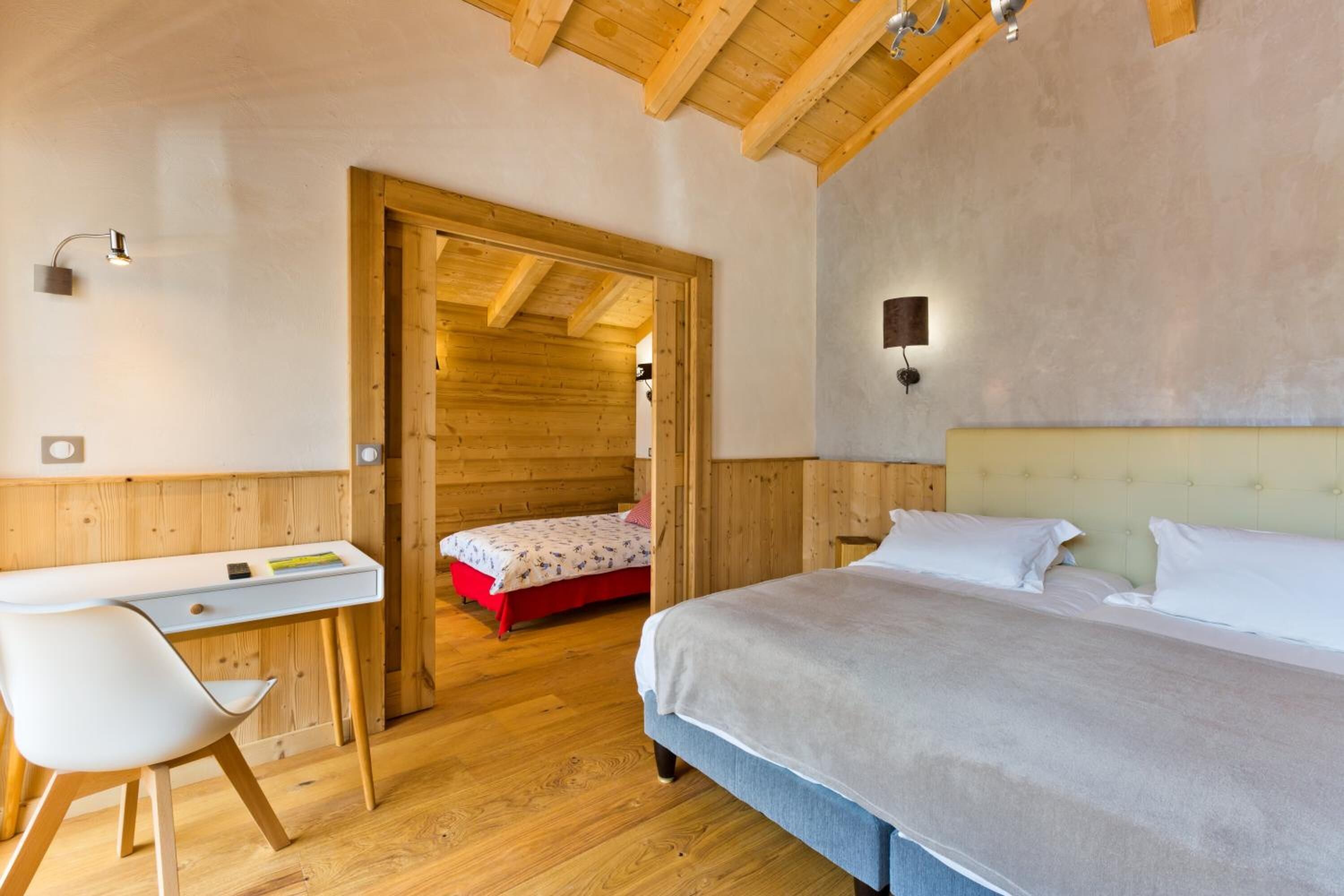 Un dormitorio con techo de madera, una cama, un escritorio y una silla.