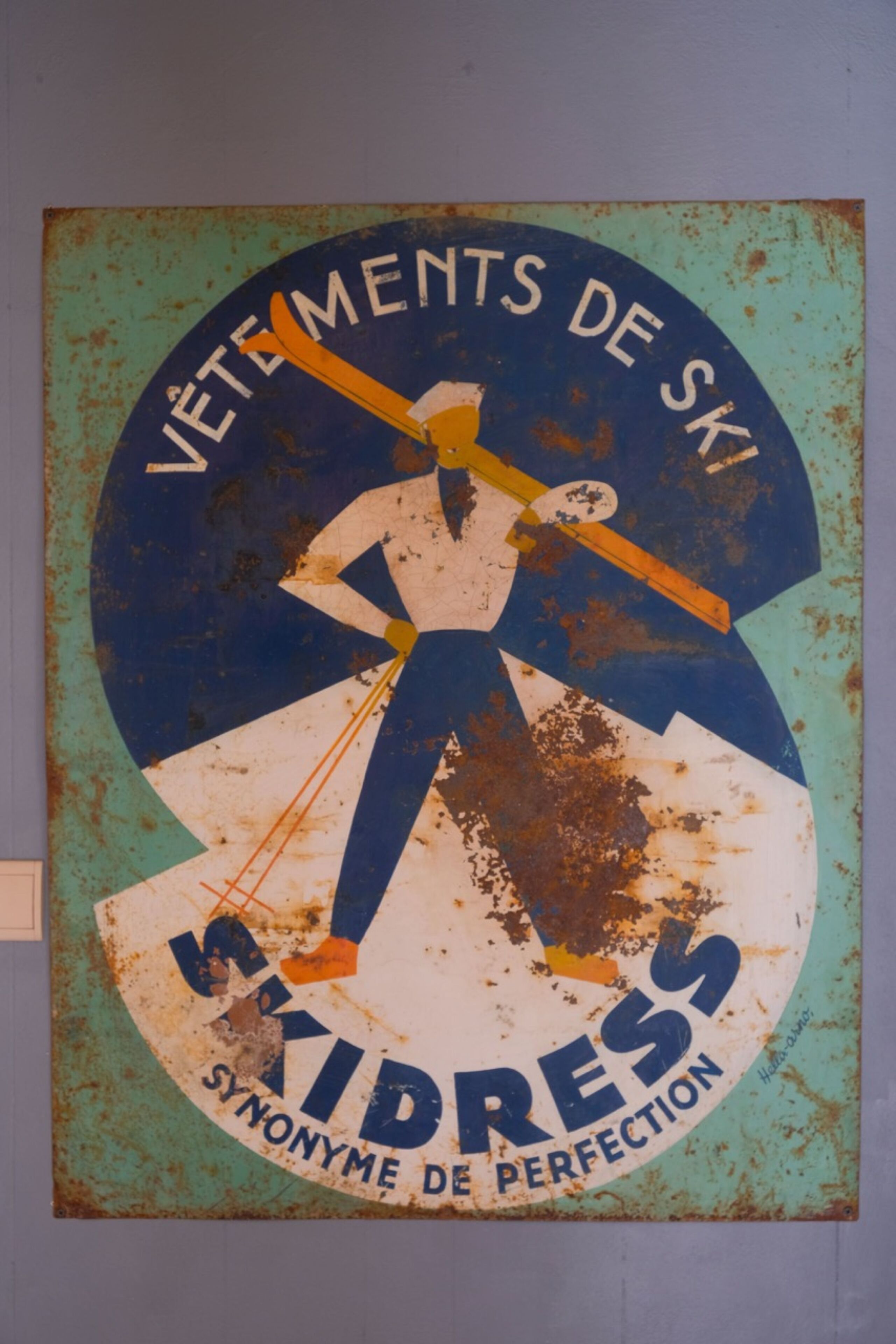 Ein Vintage-Schild mit einem Skifahrer und dem Text "Vêtements de Ski" und "Synonyme de perfection".