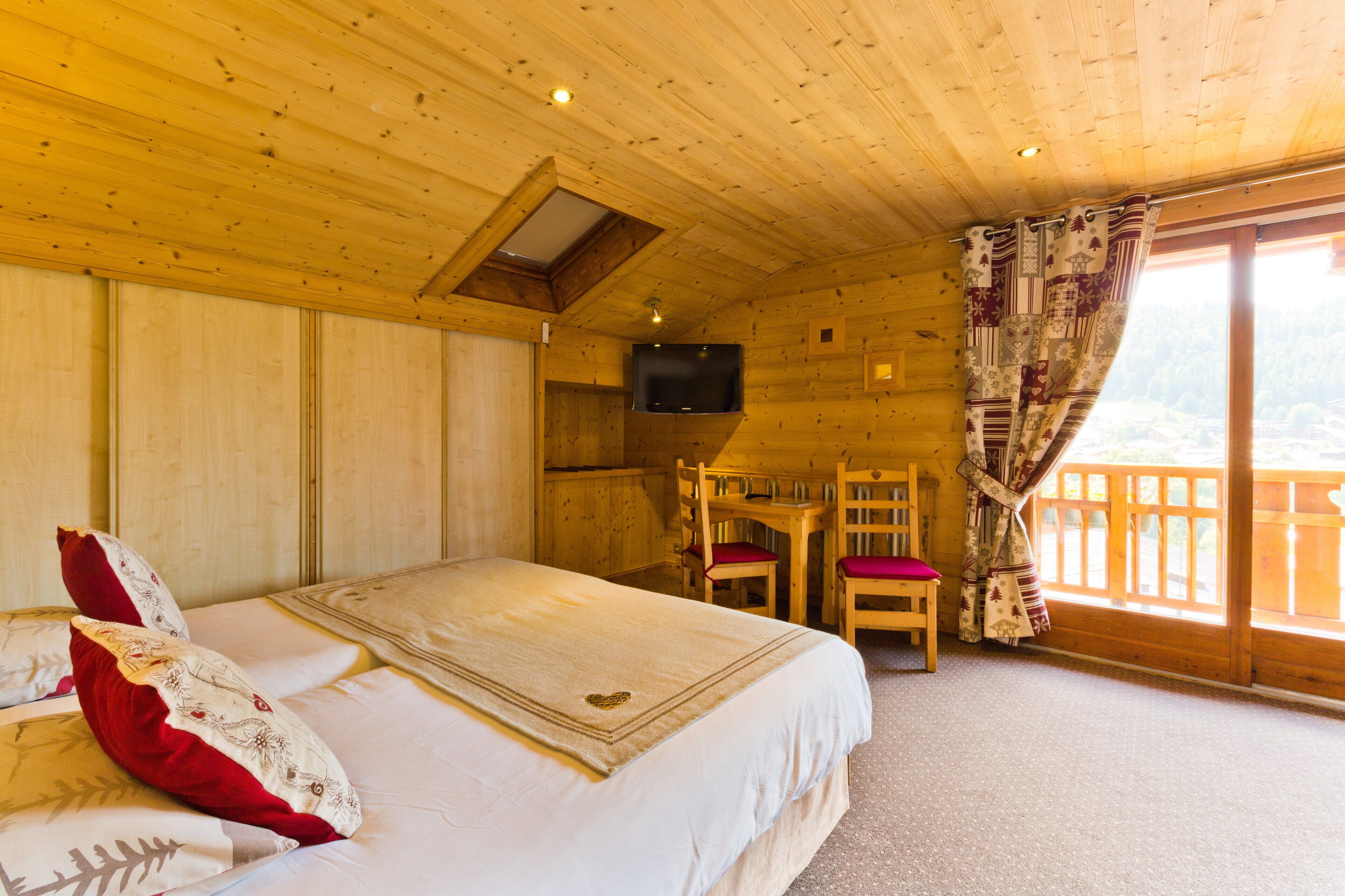 Quarto de cabana de madeira com cama, escrivaninha, cadeira e televisão.