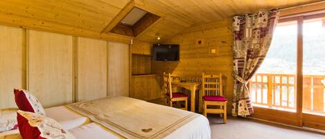 Quarto de cabana de madeira com cama, escrivaninha, cadeira e televisão.