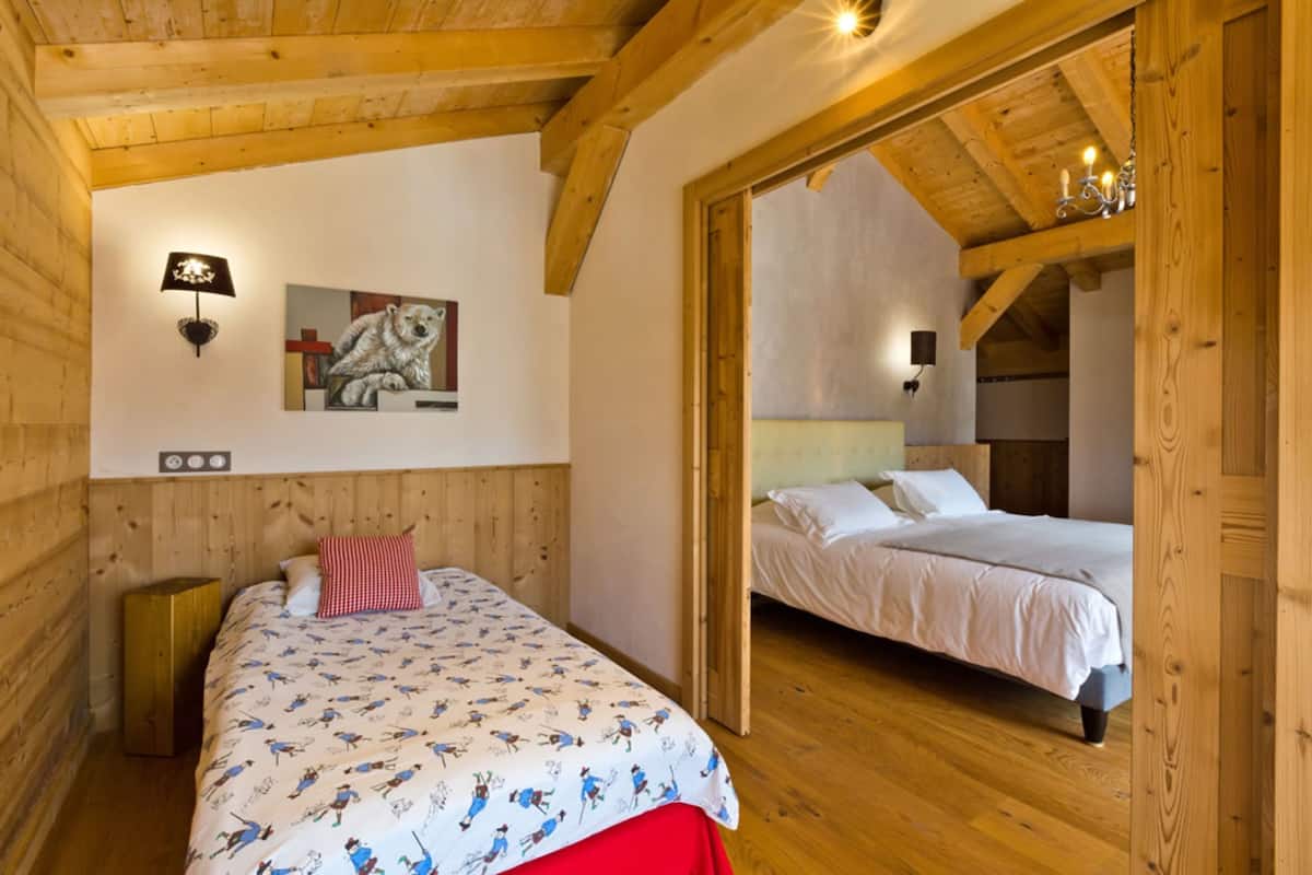 A wooden cabin bedroom with two beds, a wall-mounted lamp, and a painting of a dog.