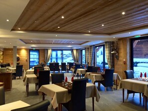 Ein Restaurant mit Holzbalkendecke, gedeckten Tischen und großen Fenstern mit Blick ins Freie.