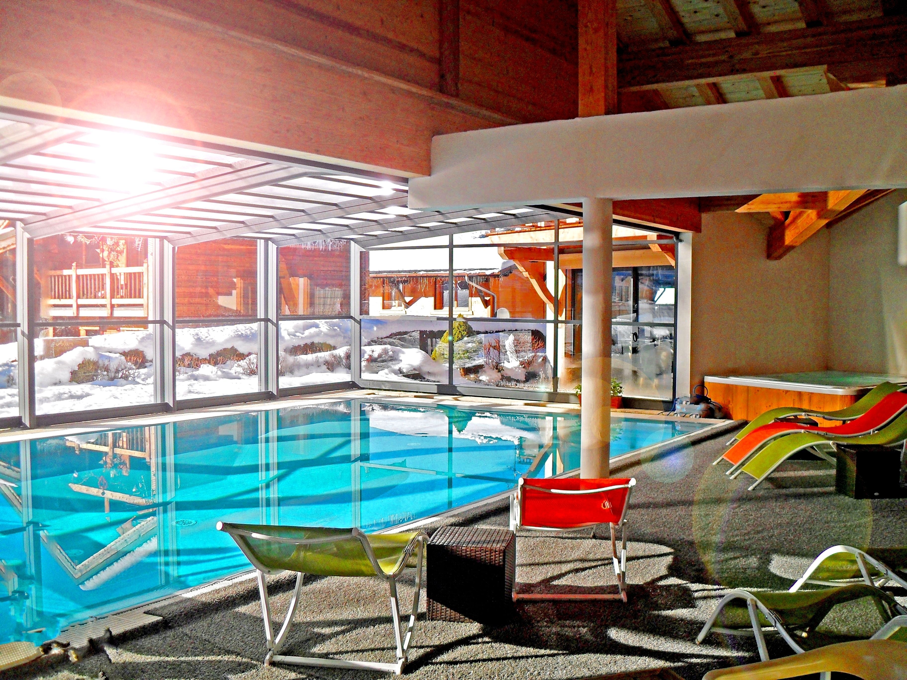 An indoor swimming pool with clear glass walls, a wooden ceiling, and a view of a snowy landscape.