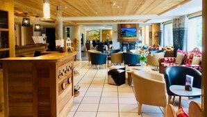 Un vestíbulo amplio con techo de madera y una zona de bar, con asientos cómodos y una pantalla de televisión.