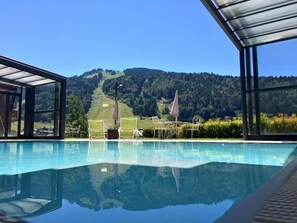 Ein Pool mit Blick auf eine Bergkulisse, einem überdachten Sitzbereich und einer gläsernen Struktur.
