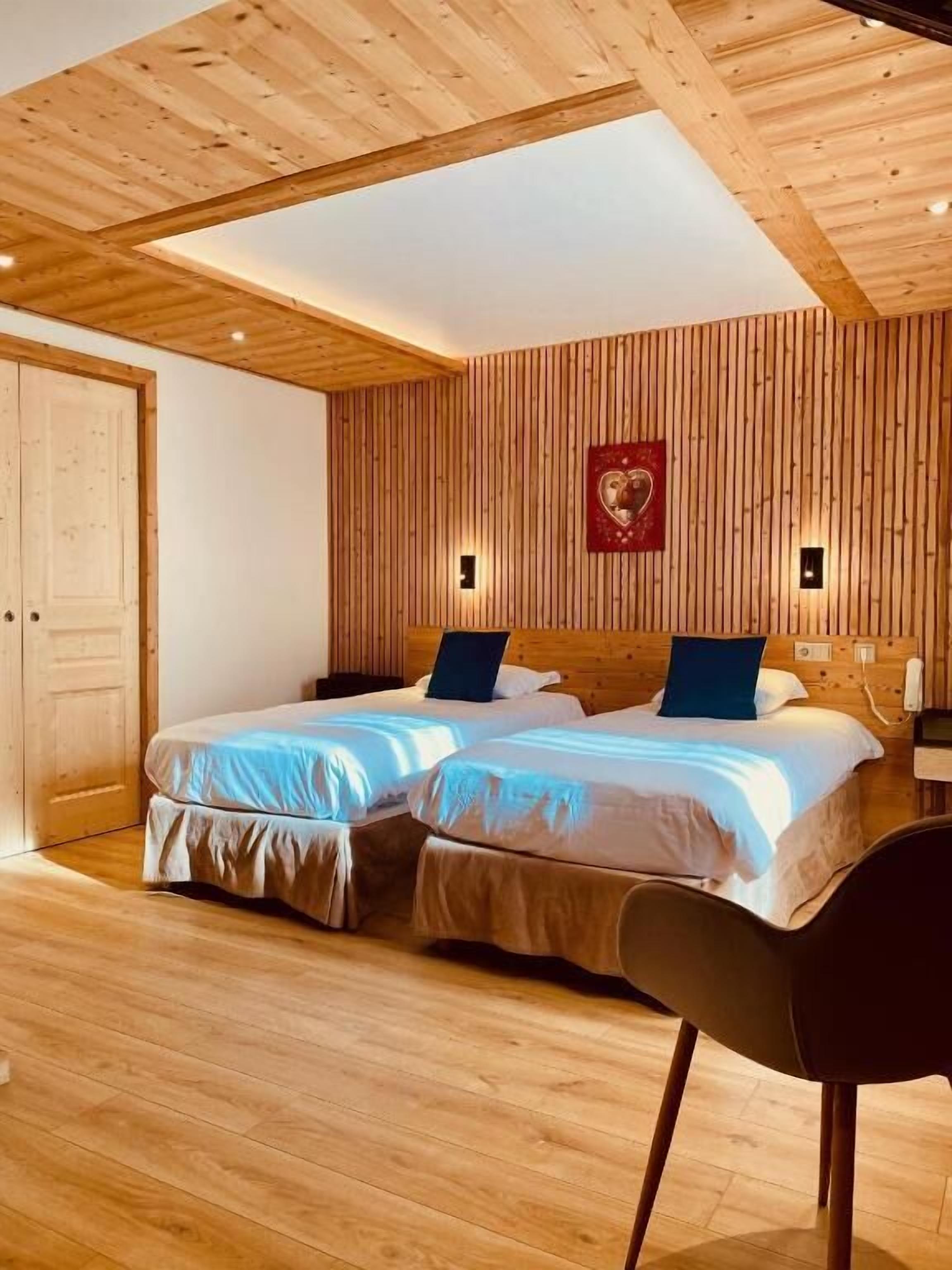 A room with two beds, wooden walls, a wooden ceiling, and a chair.