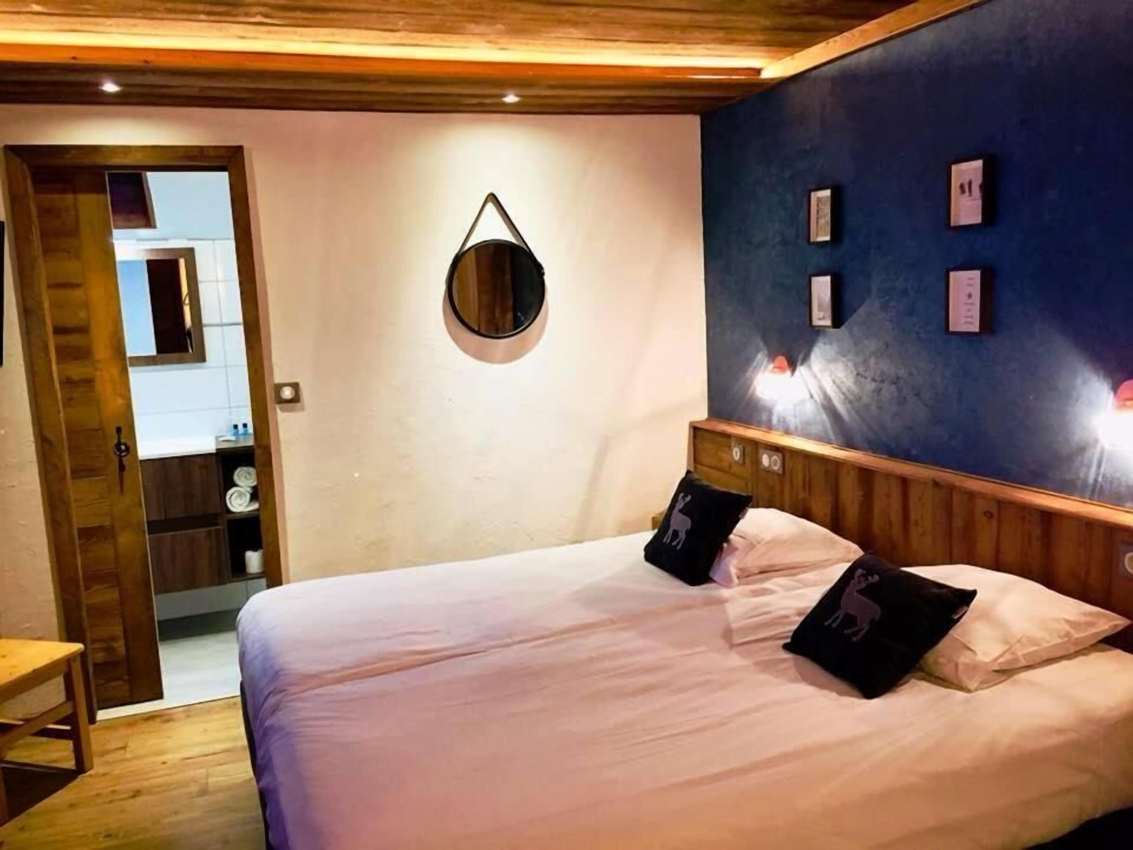 A bedroom with a bed, wooden headboard, and a wall-mounted mirror.