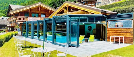 Un hôtel de style chalet doté d’un espace piscine entièrement vitré, de coins salon extérieurs et offrant une vue imprenable sur les montagnes.