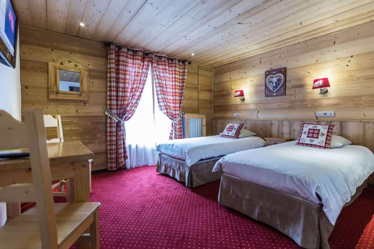 A wooden cabin room with two beds, a wooden desk, and a red carpet.