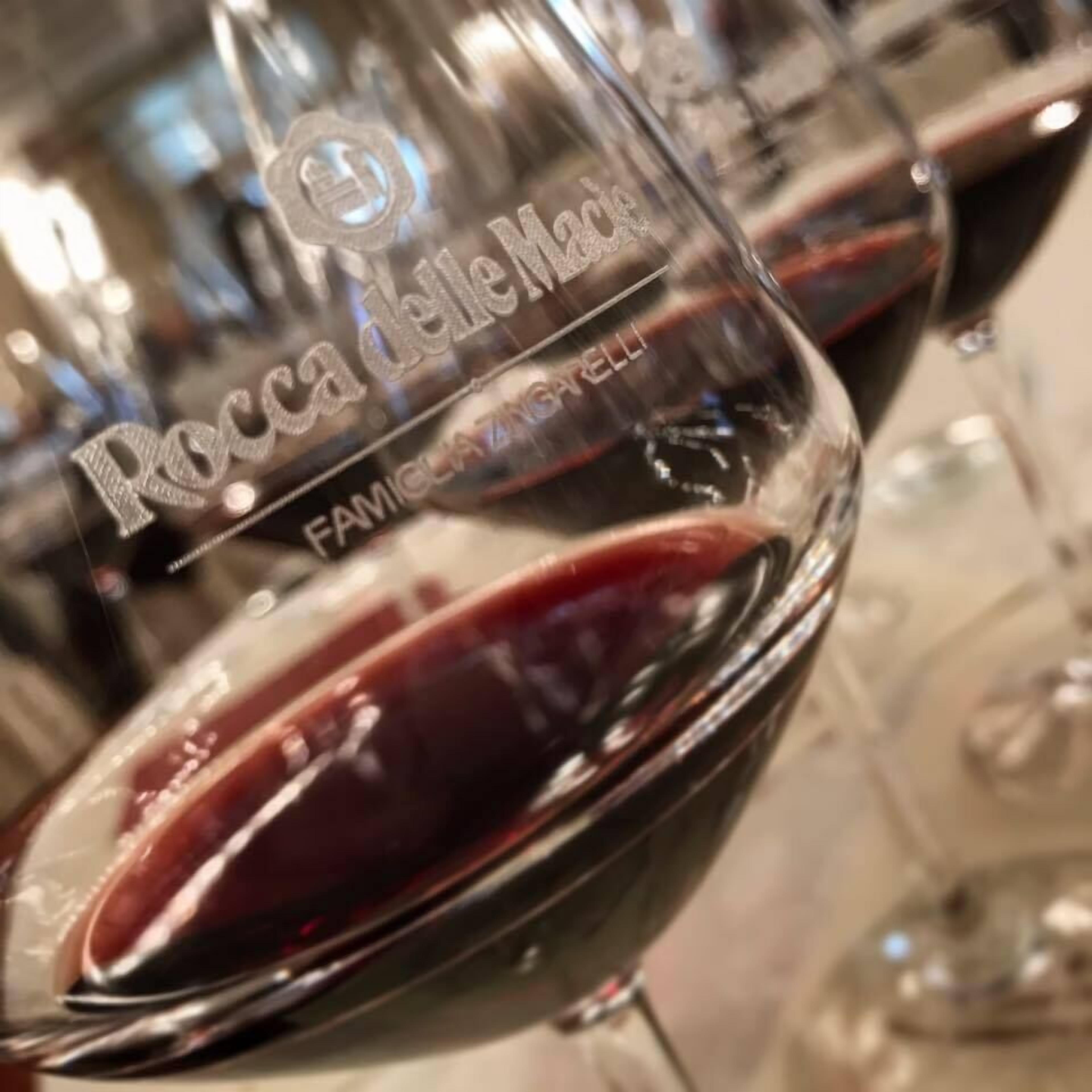 A close-up of a wine glass with the inscription "Rocca delle Marelle" and "FAMIGLIAZIONE".